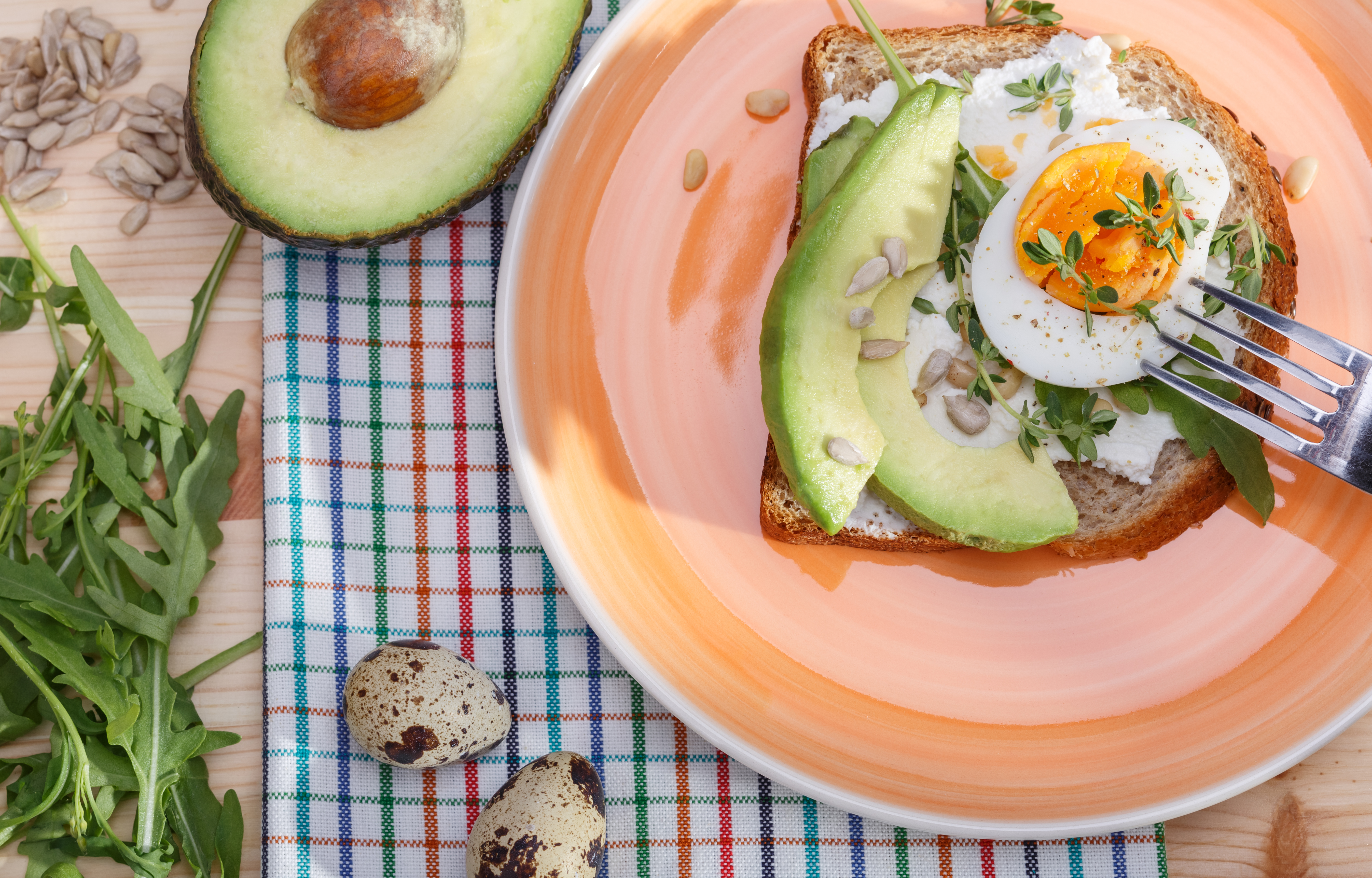 A plate with a piece of toast topped with avocado and egg, with a halved avocado next to the plate.