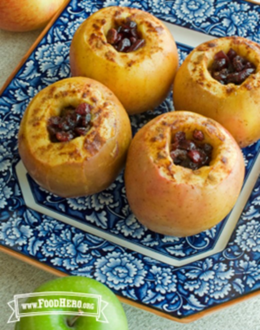 Four baked apples filled with cranberries on a decorative plate.