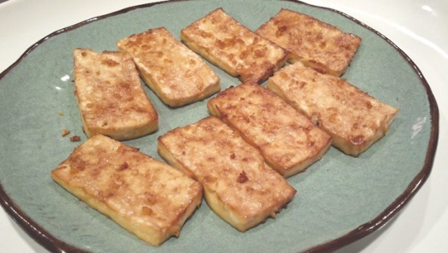 Eight slices of baked tofu on a plate. 