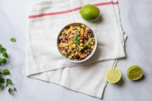 A bowl of Black Bean and Couscous Salad on a kitchen towel with two limes. 