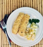 Two enchiladas on a plate with a side of fruit salsa, a lime, and cilantro.