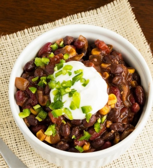 A bowl of chili topped with sour cream and green peppers. 