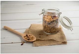 A glass jar with a wooden spoon containing Cranberry Pecan Granola.