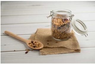 A glass jar with a wooden spoon containing Cranberry Pecan Granola.