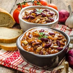 Two bowls containing Chili with a side of bread.