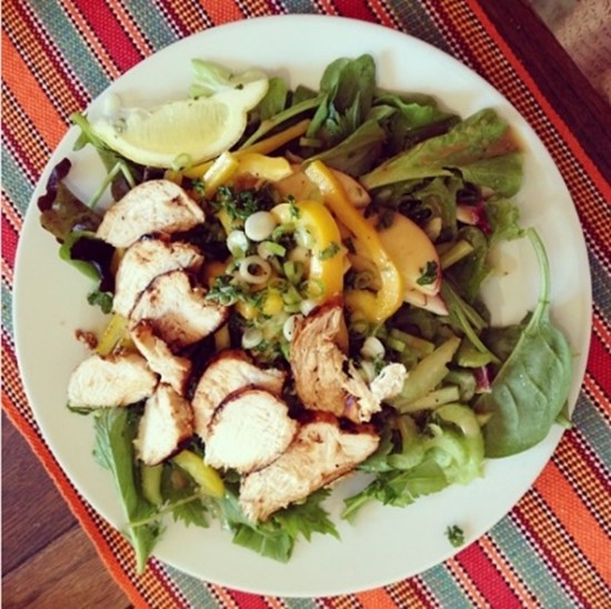 A bowl of salad topped with chicken, vegetables, and a lemon slice.