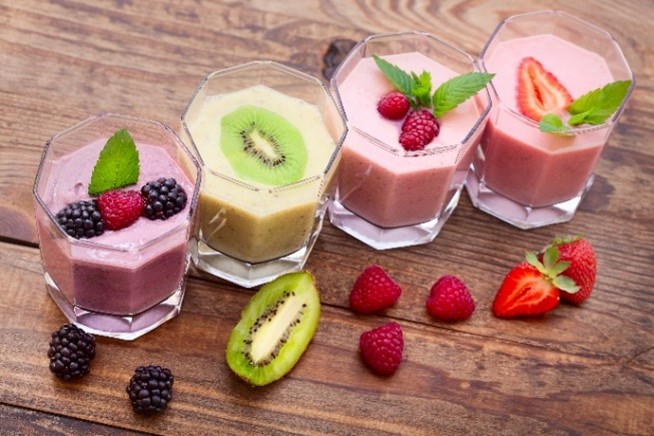Four smoothies topped with blackbarries, kiwi, raspbarries, and strawberries.
