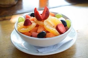 A bowl of Easy Fruit Salad, containing green and purple grapes, strawberries, and oranges.