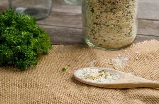 A wooden spoonful of Eating Smart Seasoning Mix next to a bunch of parsley and a jar of the seasoning mix.