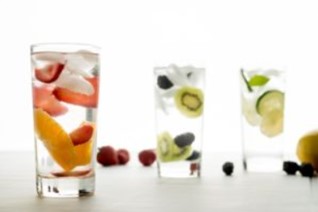 Three glasses of flavored water containing strawberries, oranges, berries, kiwis, cucumbers, and lemons.