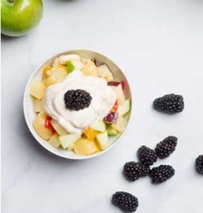 A bowl of fruit salad topped with yogurt and a blackberry.