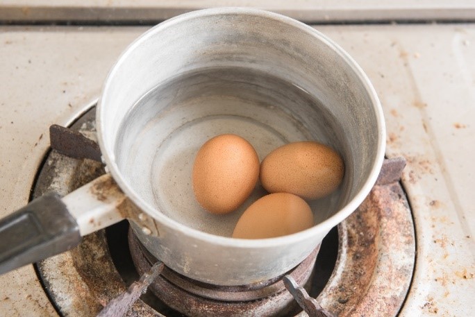A pot on a stove top holding three brown eggs in water.