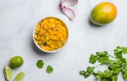 An image od mango salsa in a bowl next to a whole mango, cilantro, and limes.