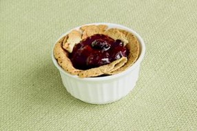 An image of a mini berry pie in a white bowl with a red berry filling.