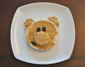 An image of a rice cake with peanut butter and raisins in the shape of a bear's face.