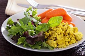 Scrambled tofu on a white plate next to baby carrots and a salad.