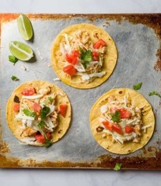 An image of three tortillas on a baking sheet with fish, cilantro, and tomatoes.