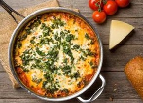 An image of skillet lasagna on a table next to a wedge of cheese, tomatoes, and a piece of bread.