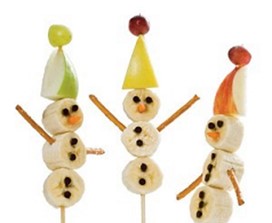 An image of three snowmen on a stick with apples and grapes as a hat, three banana slices, pretzels for arms, sliver of a carrot for a nose, and mini chocolate chips for buttons and eyes.