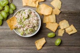 An image of tuna salad in a bowl on a wooden surface with crackers and grapes. placeholder image