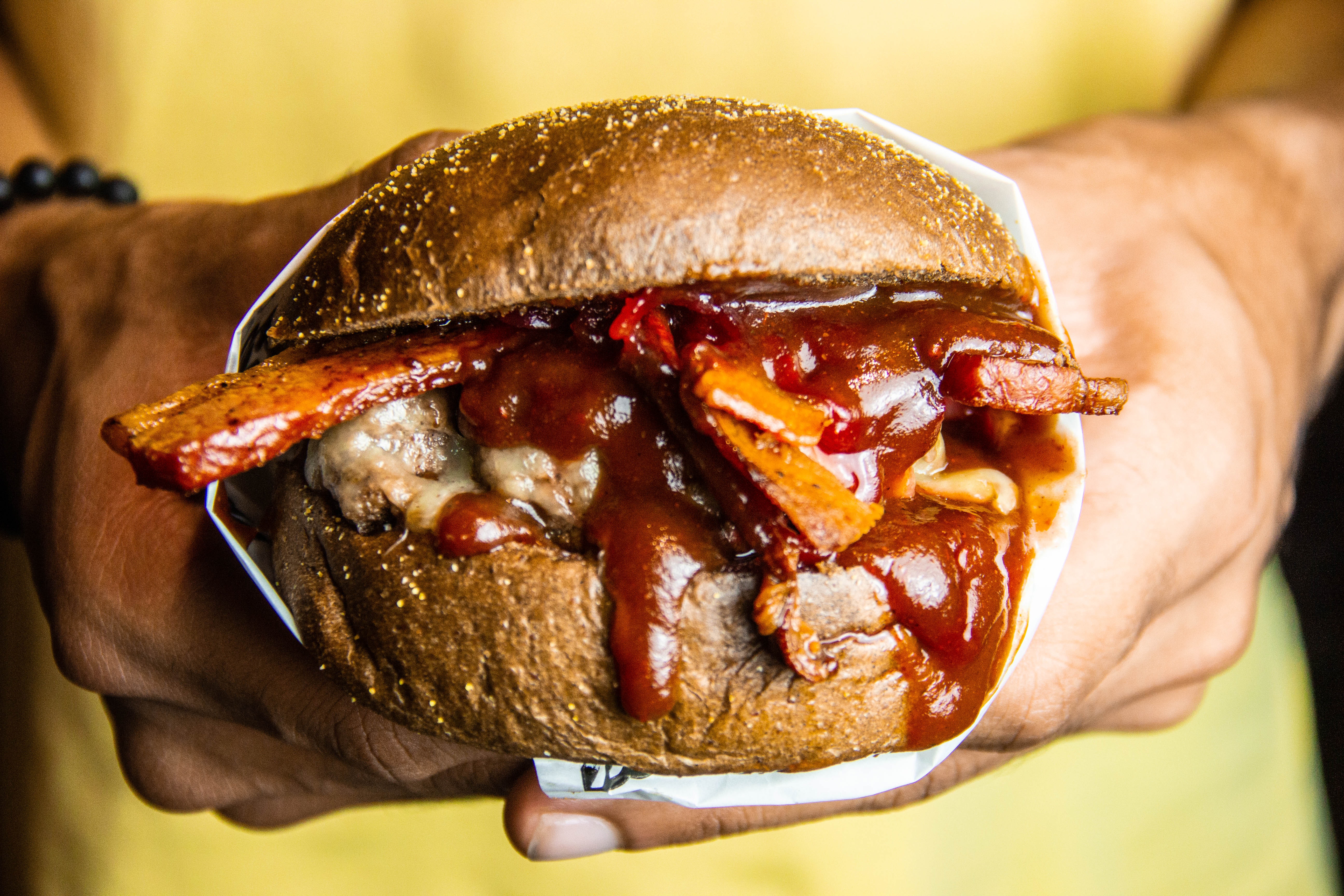 person in a yellow shirt holding a grilled cheeseburger dripping with bbq sauce
