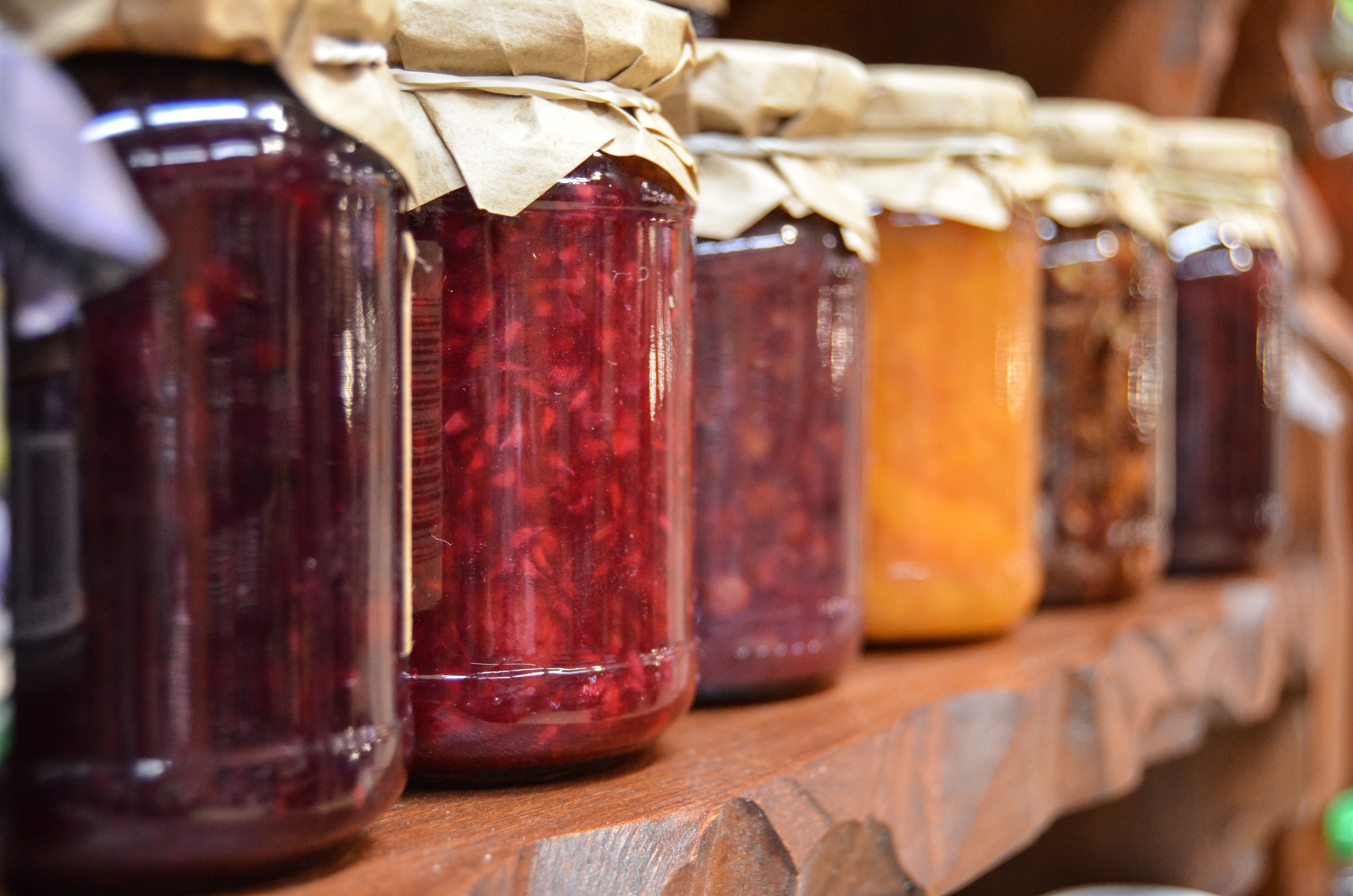 jams and jellies on a shelf canned food in glass jars with cloth lids sitting on a wooden shelf