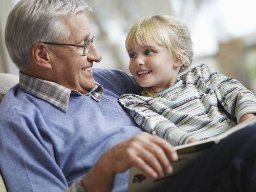 Happy little girl sitting on Grandpa's lap while reading a book.