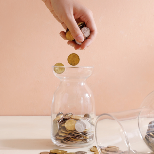 Photo of a person dropping coins into a coin jar.
