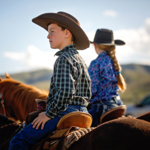 Young boy and little girl sit horseback looking off into the distance.