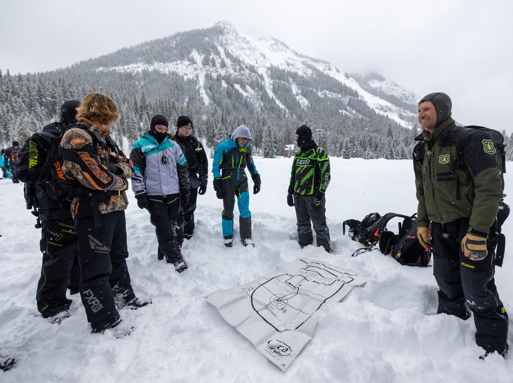A group of people stand in the snow during an avalanche training session 