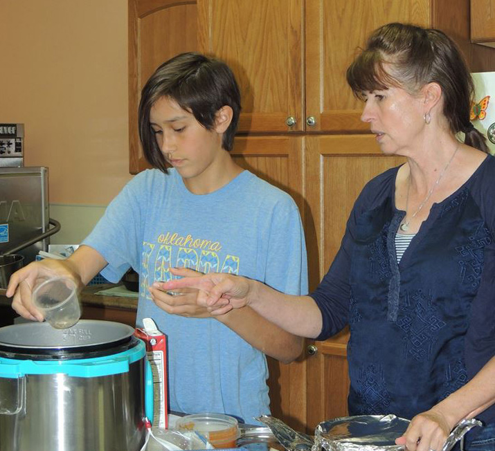 An adolescent and a woman measure ingredients to go into a large stock pot