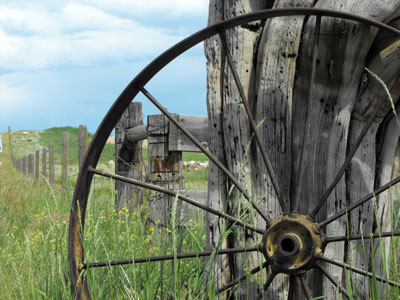 Decorative landscape photo featuring an old spoked wheel leaning on a fence