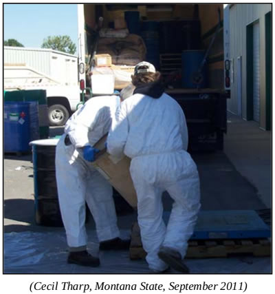 photo, two people in PPE suits move a barrel