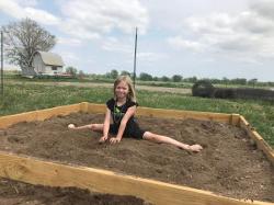Little girl doing splits in garden plot
