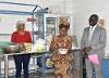 The instructor of the fermentation training stands behind a table featuring various ingredients. A woman participant mixes something in a bowl. A man is interpreting the content from English to Wolof.