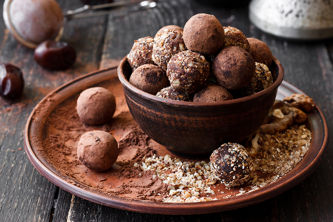 chocolate energy bites in shape of balls fill a bowl and are covered with either cacao powder or coconut