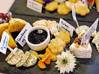 serving boards containing brie, butter, herbed crackers, grapes, and edible flowers