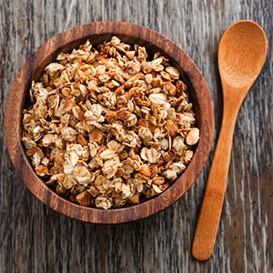 granola in bowl with wooden spoon on table next to it