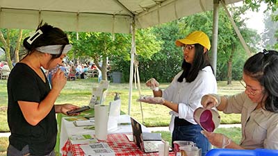 a sensory testing participant sniffs a smoothie sample for evaluation while graduate students provide instruction