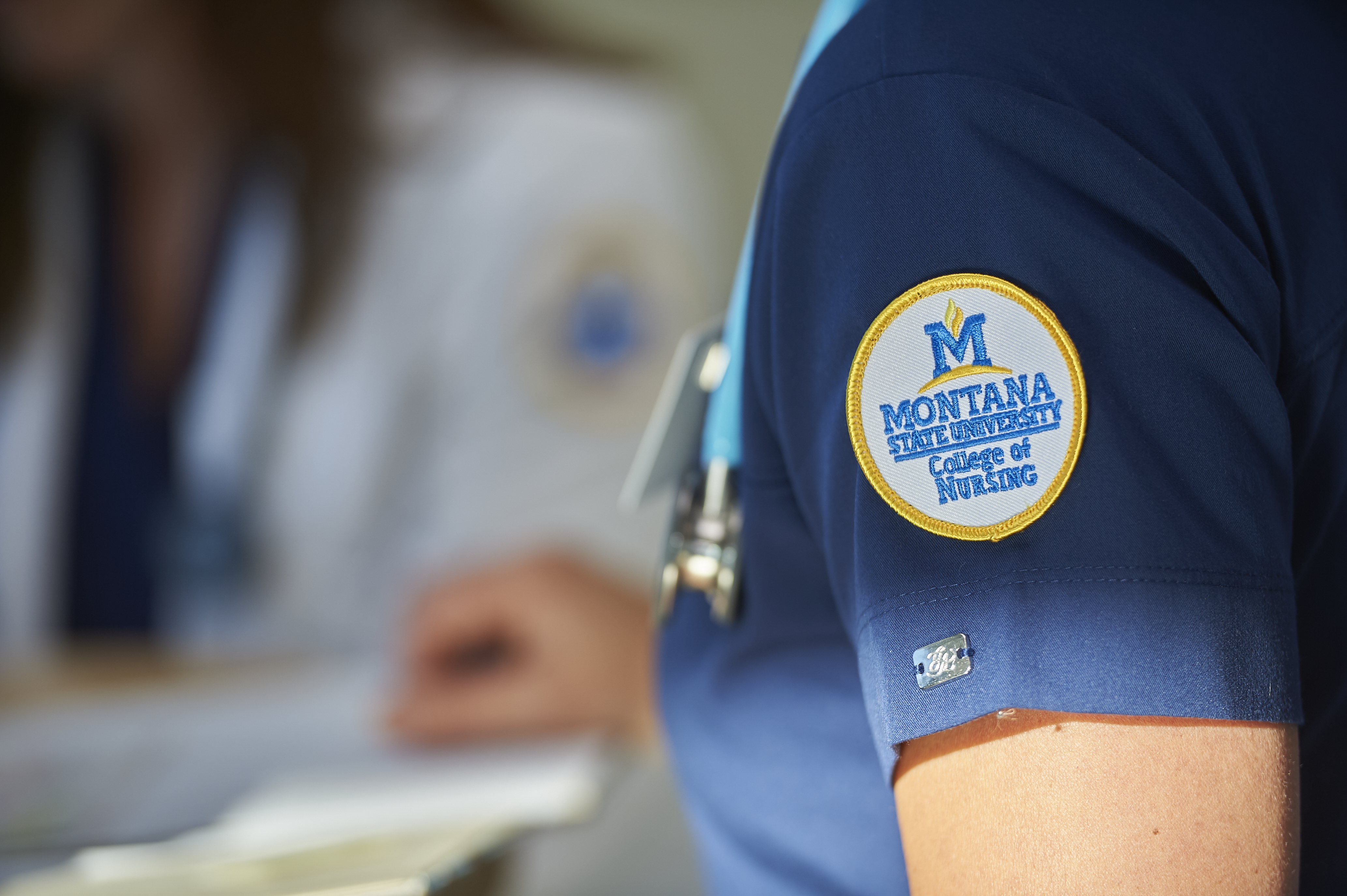 picture of arm wearing blue scrubs and college of nurse badge