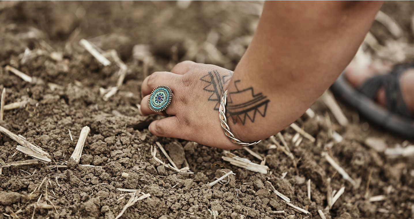 Image of woman's hand with blackfeet symbol tattoos and turquoise ring planting seeds