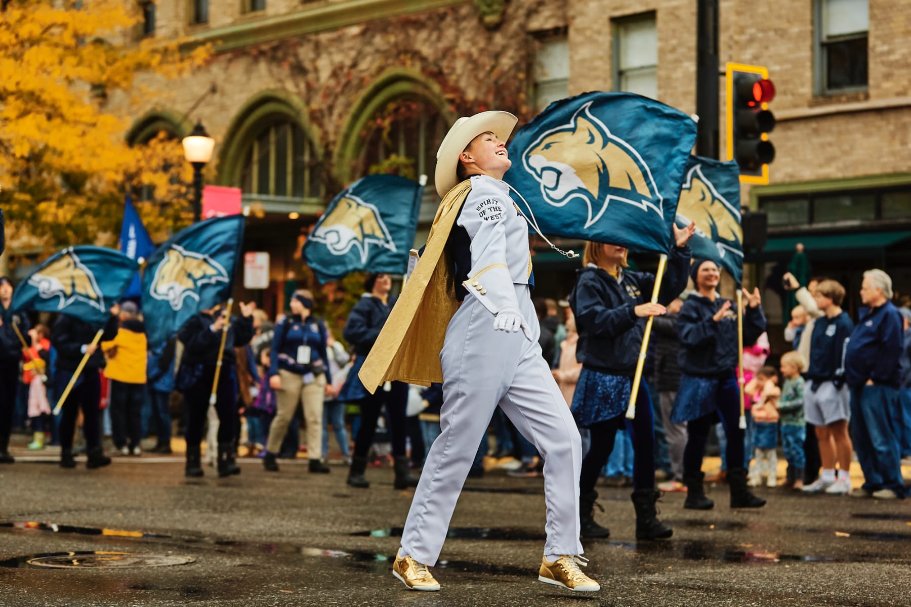 People walk down a wet city street carrying flags in a homecoming parade.