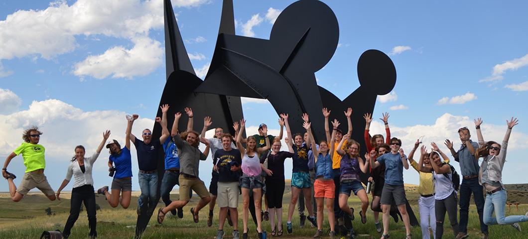 Students jumping excitedly in front of a modern metal sculpture