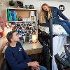 Two students in a North Hedges double room - one sits in a chair at the desk and the other sits on a lofted bed.  