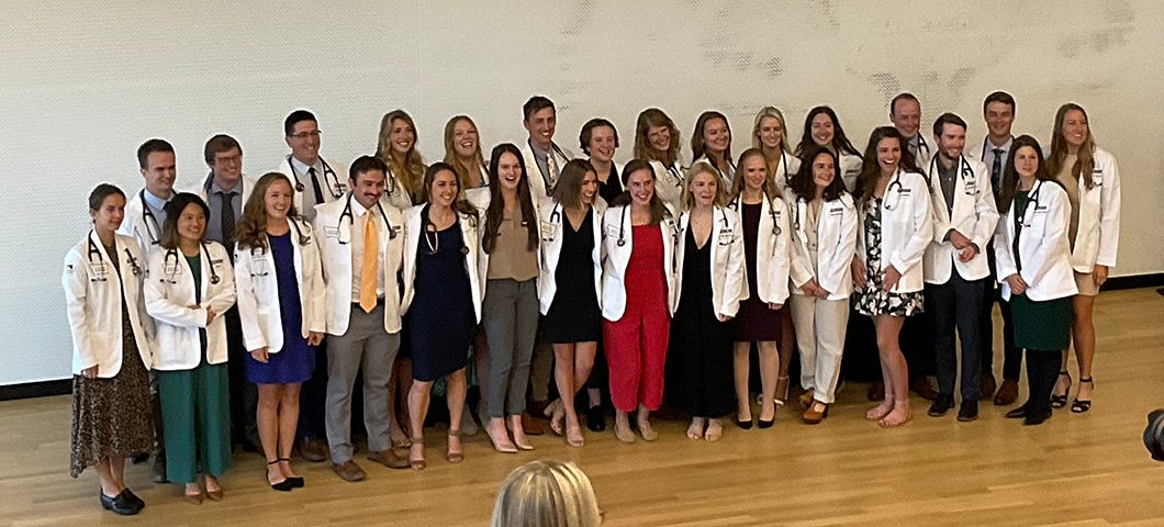 HPA students wearing lab coats and stethoscopes, standing on a wooden stage