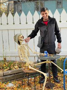 A man giggles while putting his finger in the mouth of a skeleton amid fall leaves.