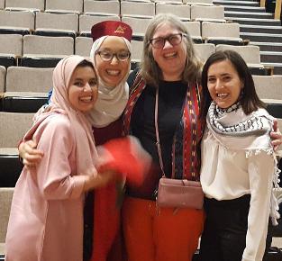 Three women in traditional outfits from their cultures pose with a local Bozeman community member, female, in front of an auditorium. They look giddy.