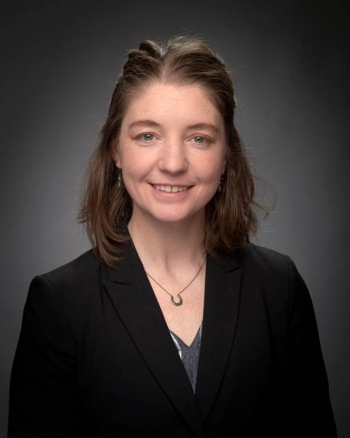 Headshot of woman, white with brown hair, in front of dark background