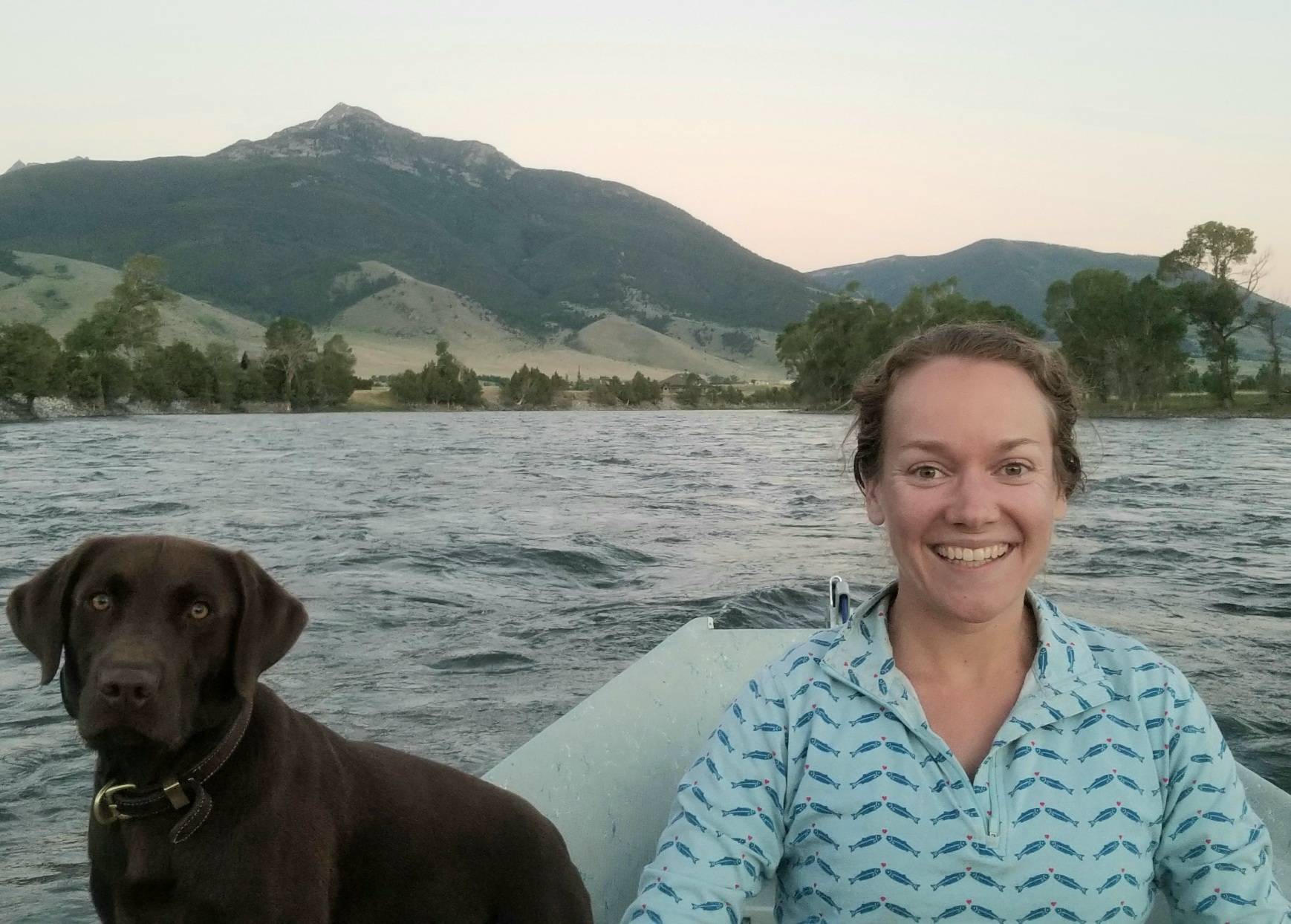 Michelle is sitting in a boat in a lake with her dog.
