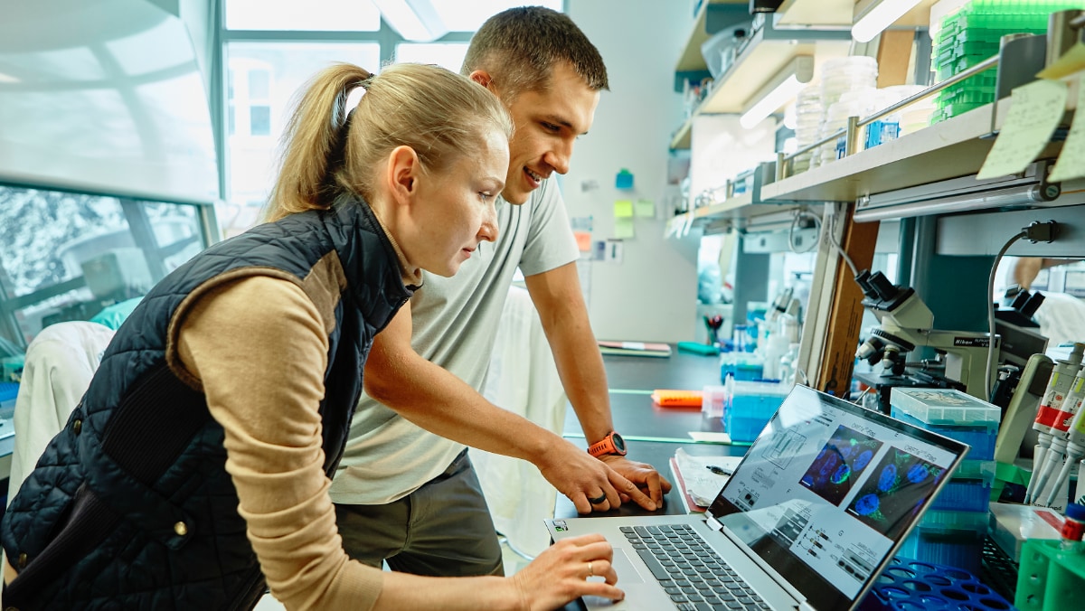 Two people in a laboratory look at a laptop together.